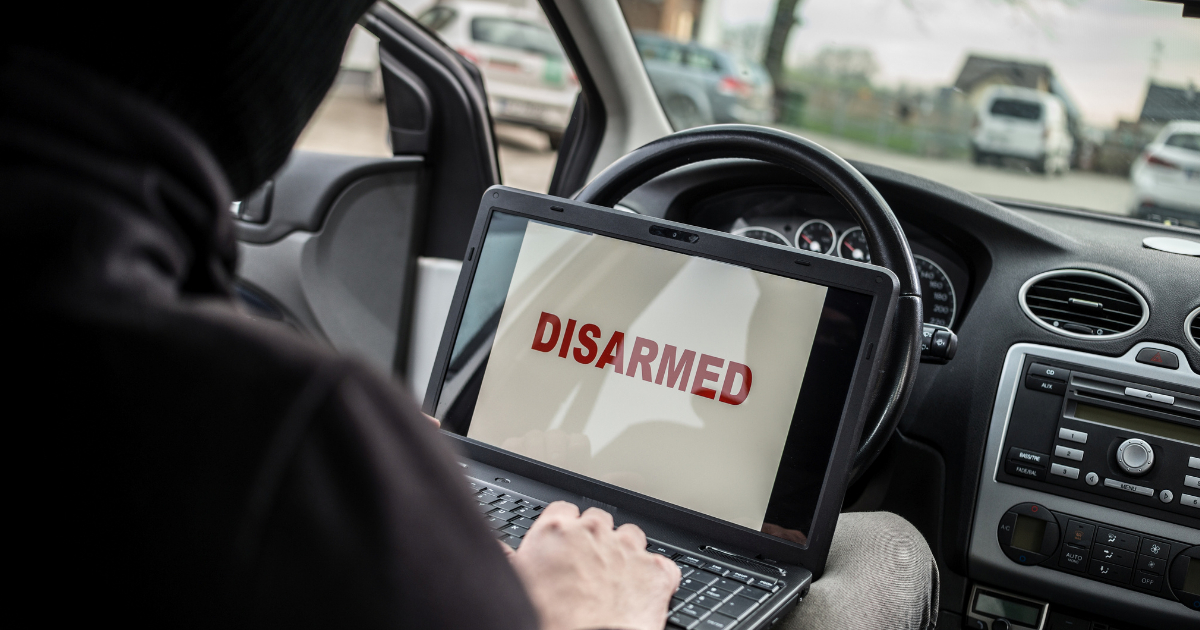 A criminal sitting in the driver's seat disabling an alarm using a laptop.